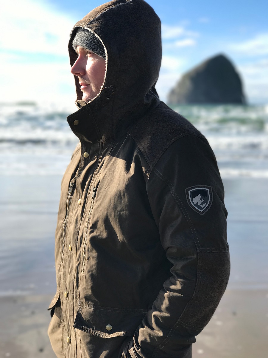 A man standing at a shore on a winter day, wearing KUHL winter hiking jacket.