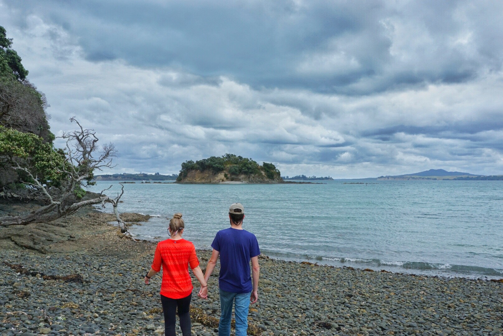 A man and a woman holding hands walking on a rocky shore on a cloudy day