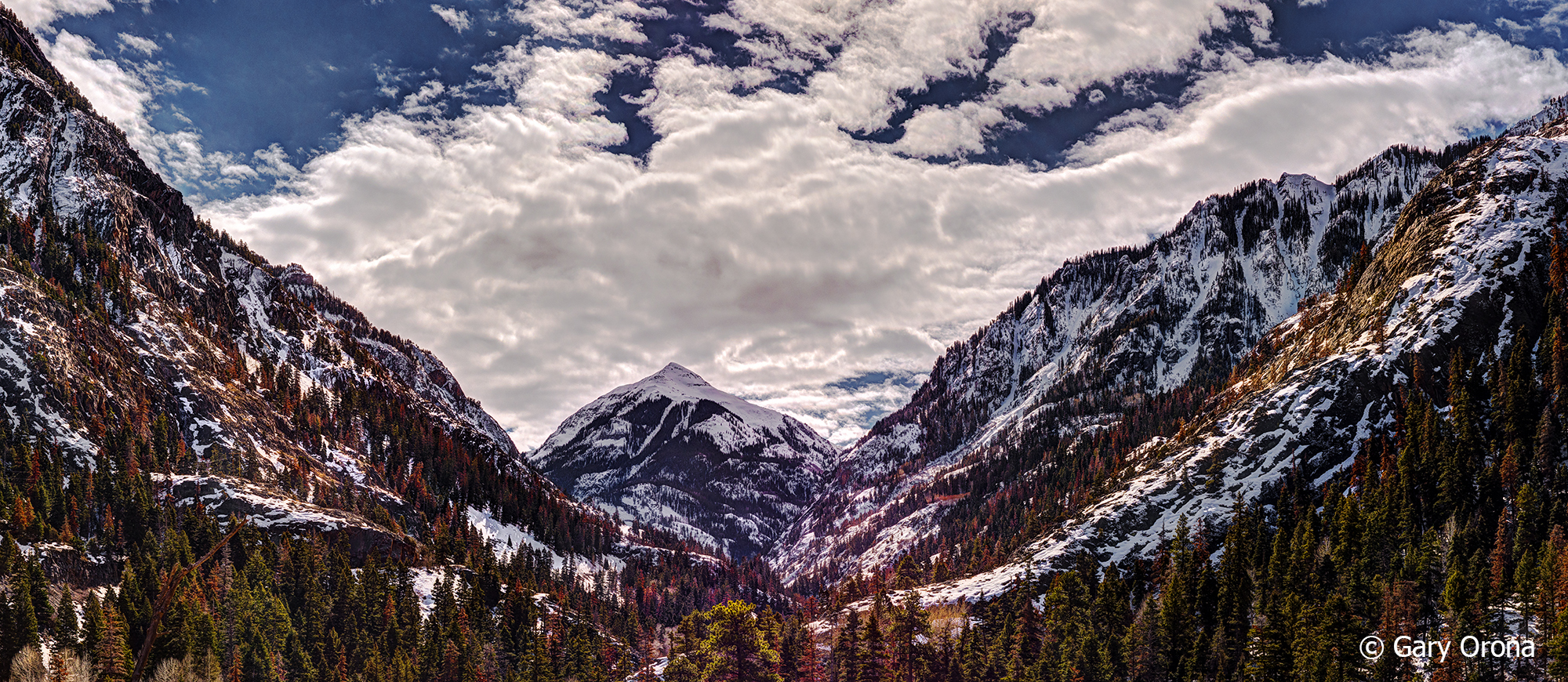A breathtaking landscape image of a snow covered mountain valley, pine forest and fluffy clouds