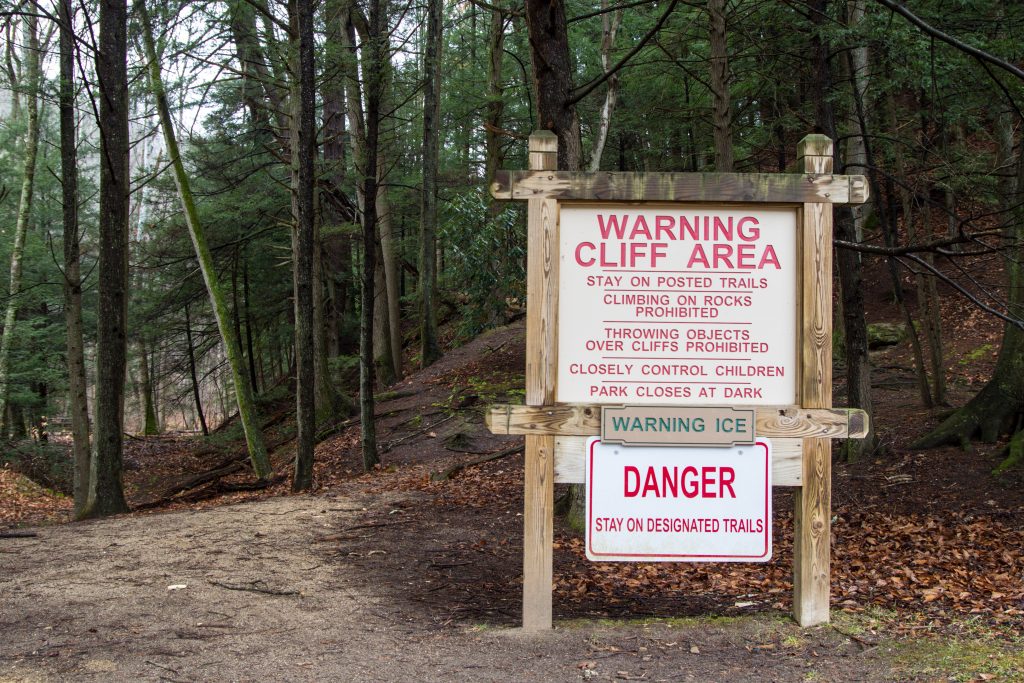 A sign next to a paved trail warning about the dangers of cliff area.