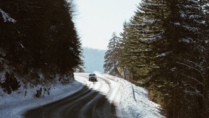 Car on snowy road surrounded by tall trees