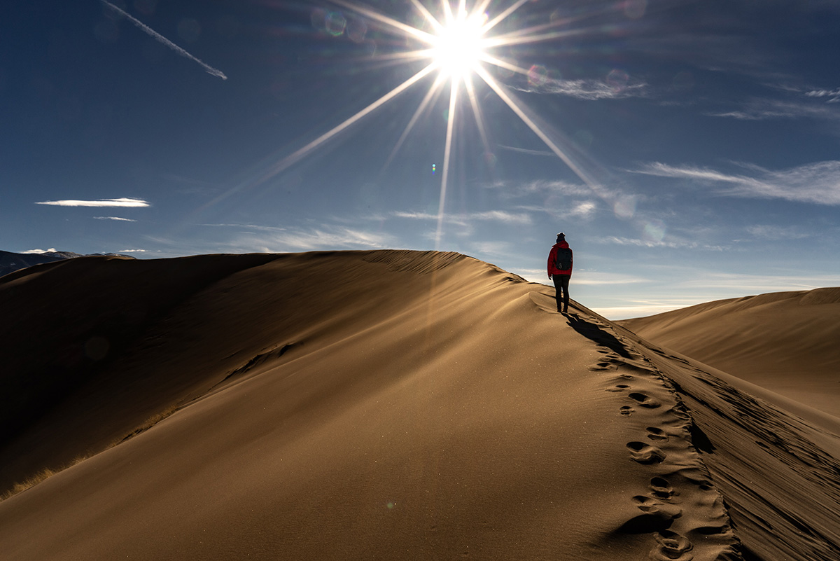 man walking on top of brown sand dune