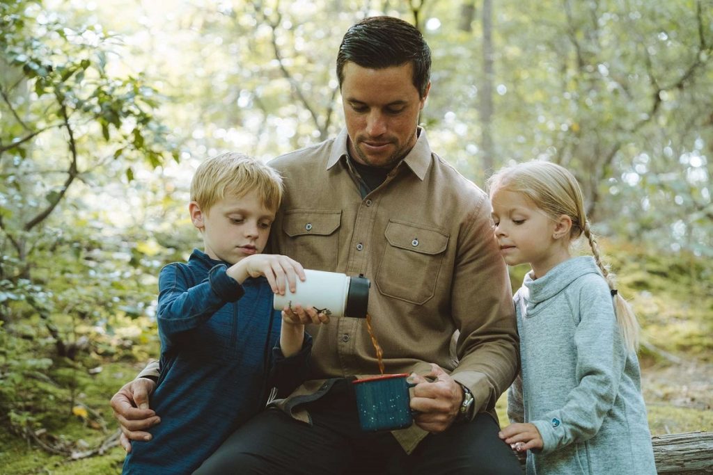 man with two kids pouring coffee on picnic