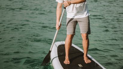 man in KÜHL shorts paddleboarding on body of water