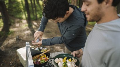 man in KÜHL shirt seasoning meal in camping stove