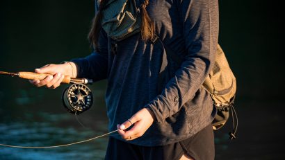 woman in KÜHL shirt holding fishing rod on lake