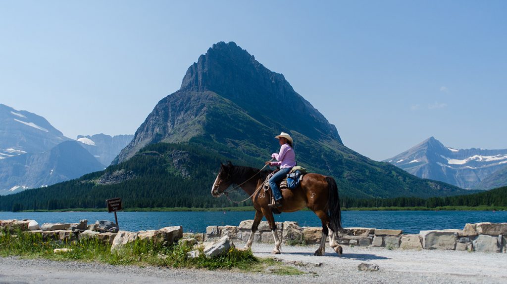 man horseback riding on trail with mountain in background
