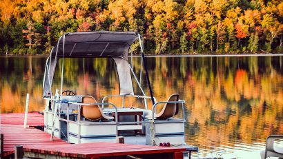 white pontoon boat on body of water with yellow trees in background