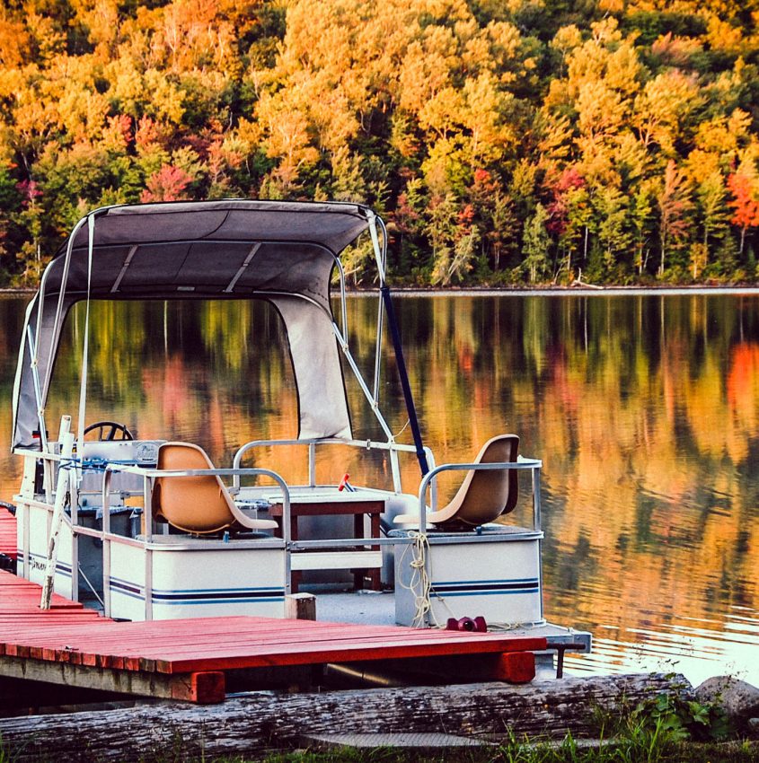 white pontoon boat on body of water with yellow trees in background