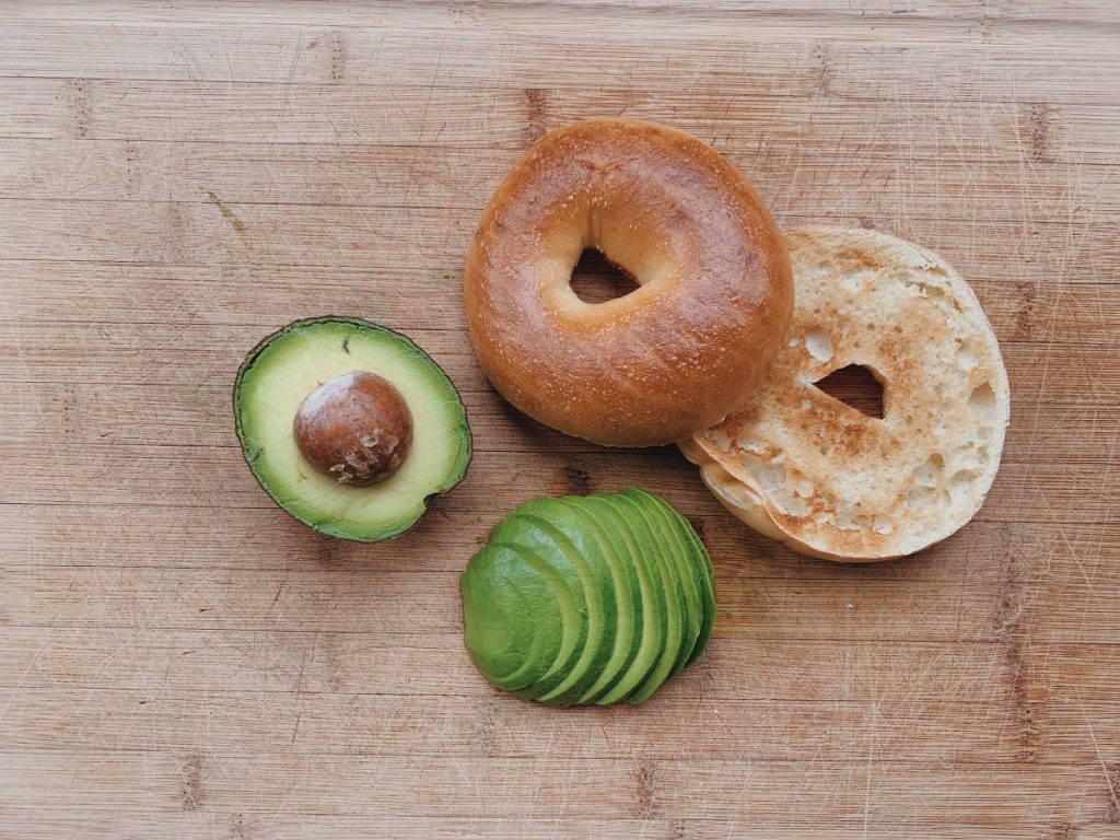 a bagel and avocado cut in half on brown board