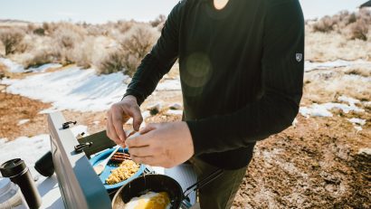 man in KÜHL long sleeve shirt cooking eggs outdoors