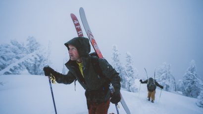 man in KÜHL jacket going uphill on skis surrounded by snow