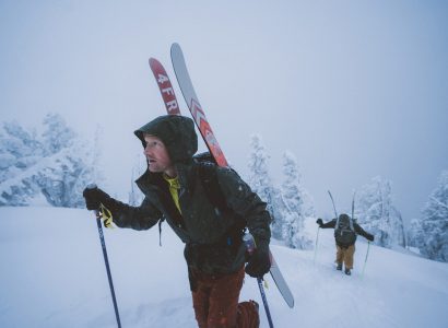 man in KÜHL jacket going uphill on skis surrounded by snow