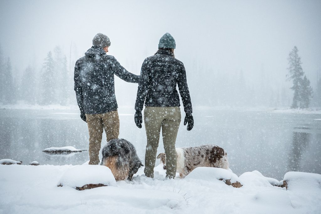 people in KÜHL clothing next to two dogs on snowy field
