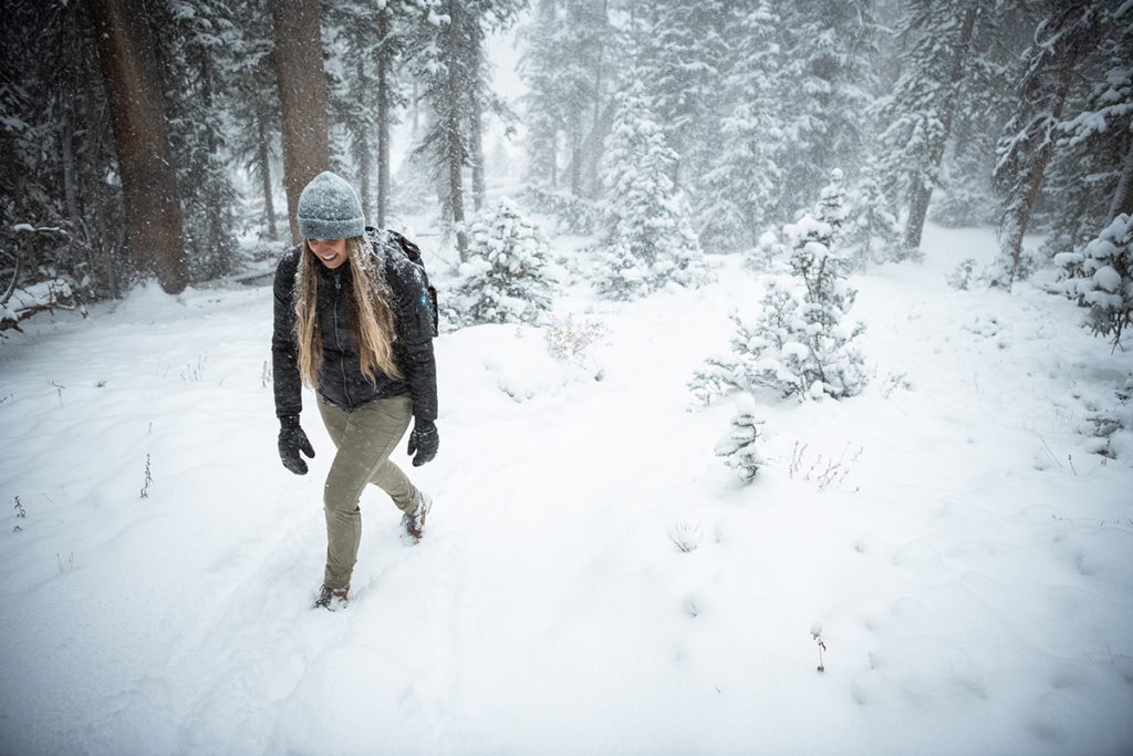 woman in KÜHL clothing walking on snowy path in the forest