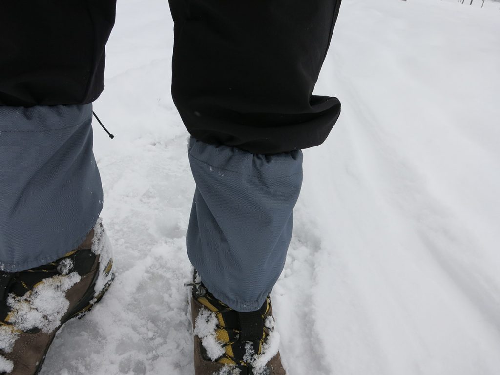 hiker wearing gray leg gaiters over black boots and pants on snow