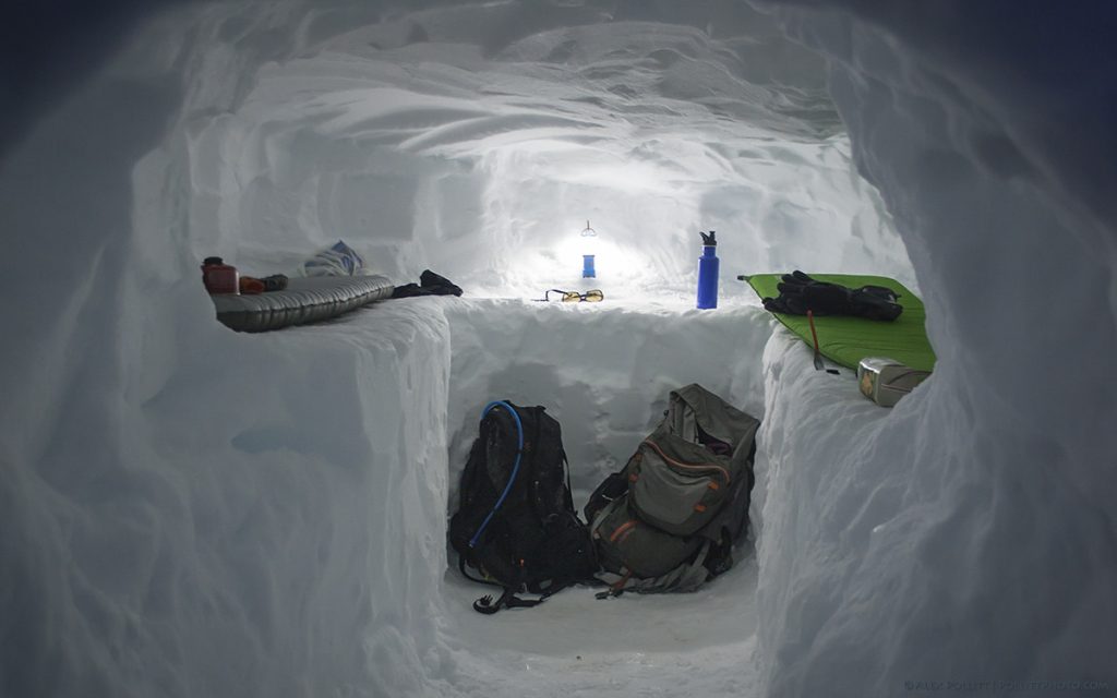 two backpacks two sleeping bags blue water bottle and sunglasses in snow cave survival shelter