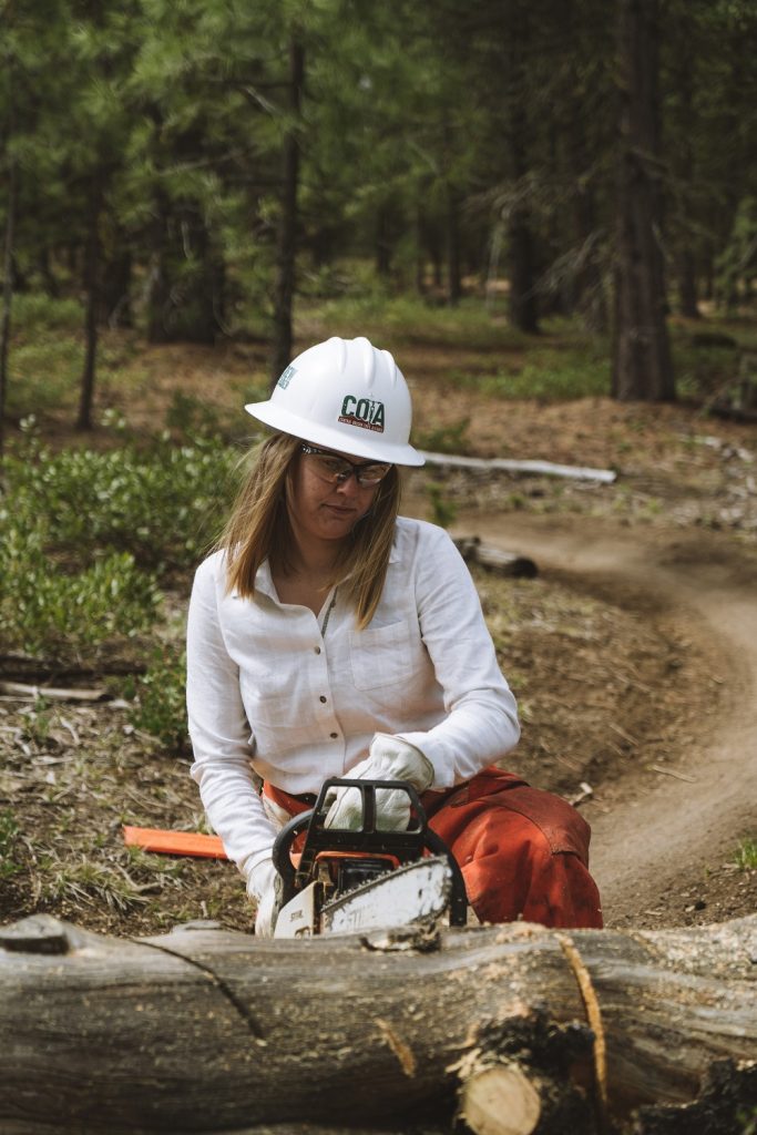Vanessa cutting down a tree while building a mountain biking trail in KUHL clothing for women
