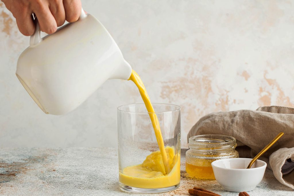 Golden milk is poured from a jug into a glass