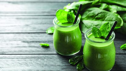 Jars of healthy green smoothie with fresh spinach on grey wooden table