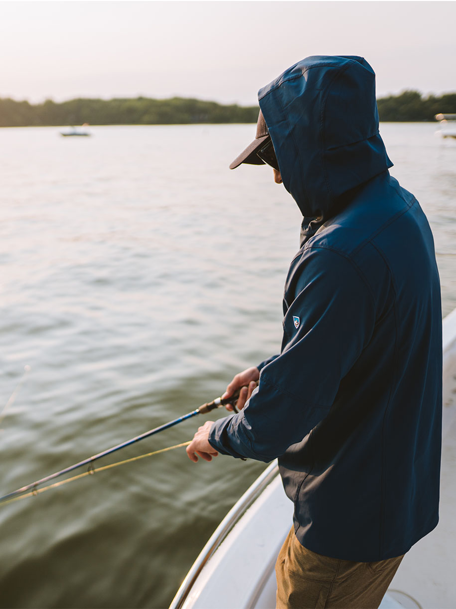 A man in fishing hoody casts a line on a boat