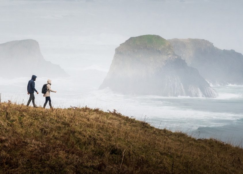 KUHL Rainwear at its best - on hikers trekking across backcountry with sea in the backround
