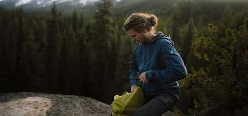 A man setting up his camping tent on a rocky terrain while wearing KUHL men's lightweight jackets